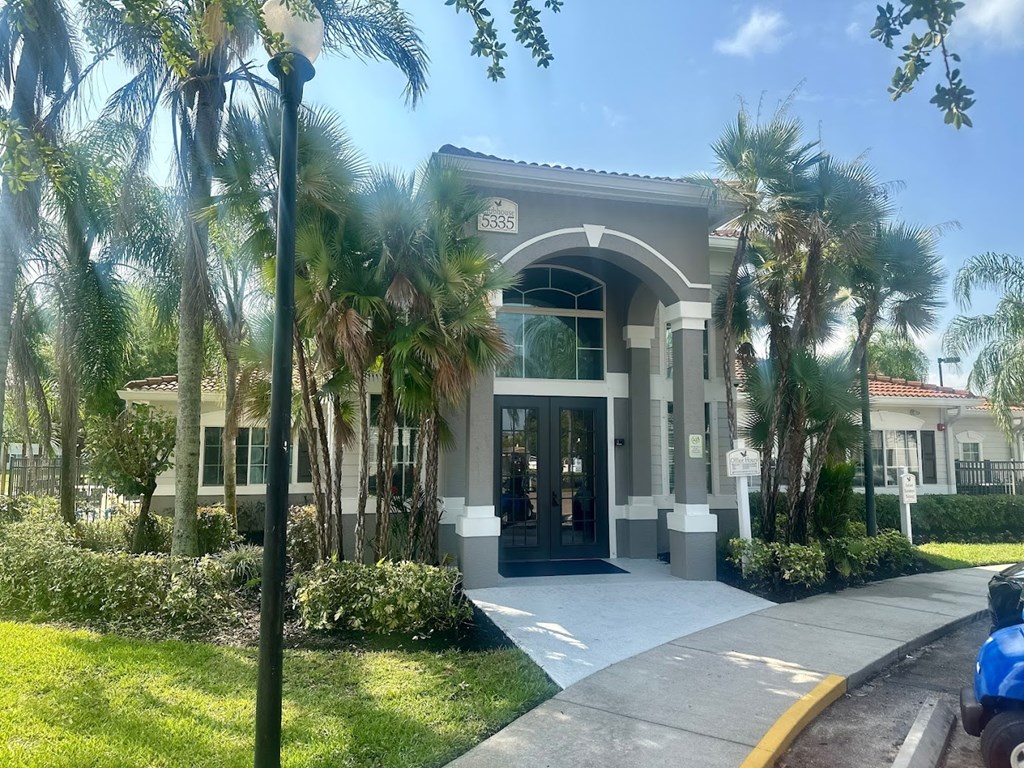 A building with a glass entrance is surrounded by palm trees at Hawk's Landing Apartments, Fort Myers, FL