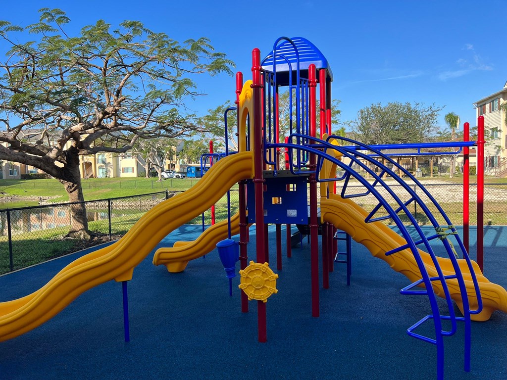 A playground with a blue and yellow slide and a red and blue tower at Hawk's Landing Apartments, Fort Myers