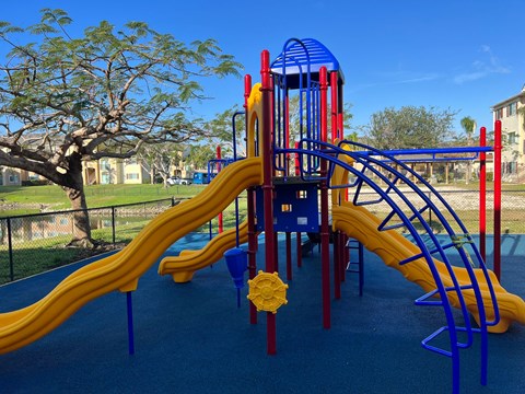 A playground with a blue and yellow slide and a red and blue tower at Hawk's Landing Apartments, Fort Myers