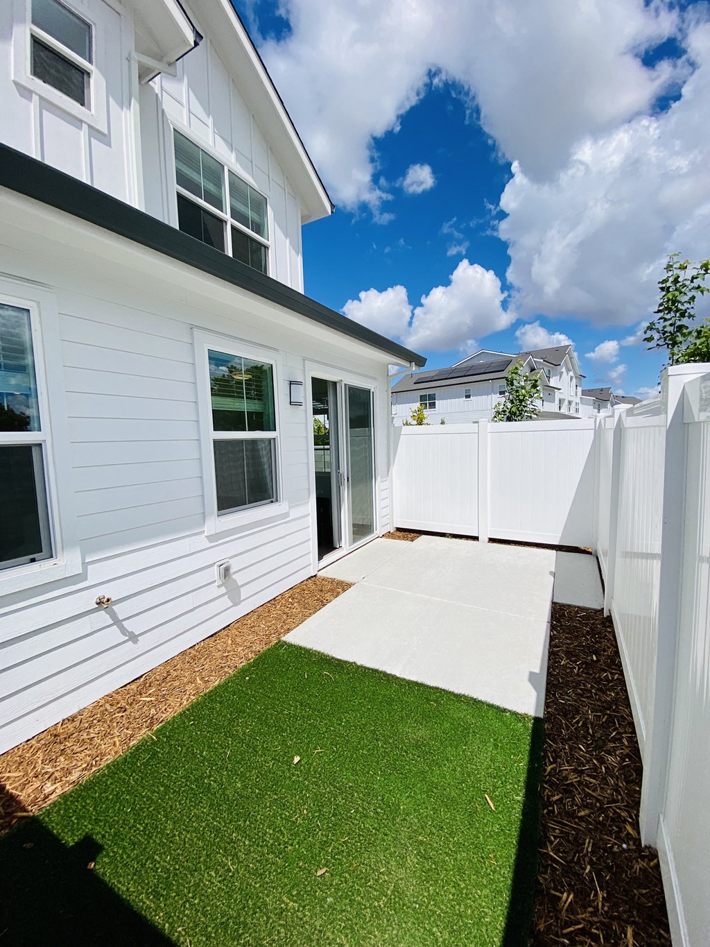 a side view of a white house with a white fence and a sidewalk and lawn