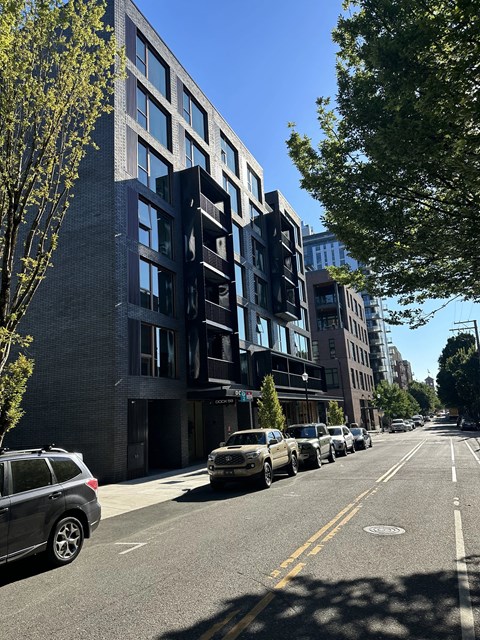 A street view of a row of modern buildings with cars parked on the side.