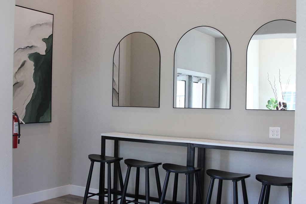 A white counter with three black stools in front of three mirrors.