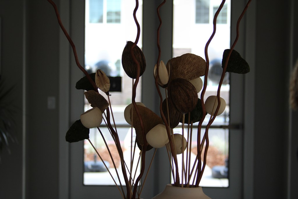 A vase with a brown and white flower arrangement sits on a windowsill.