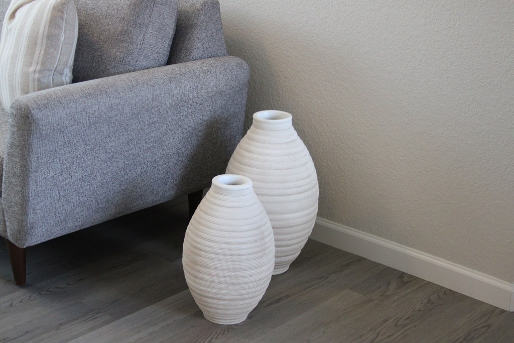 A grey couch with two white vases on the floor.