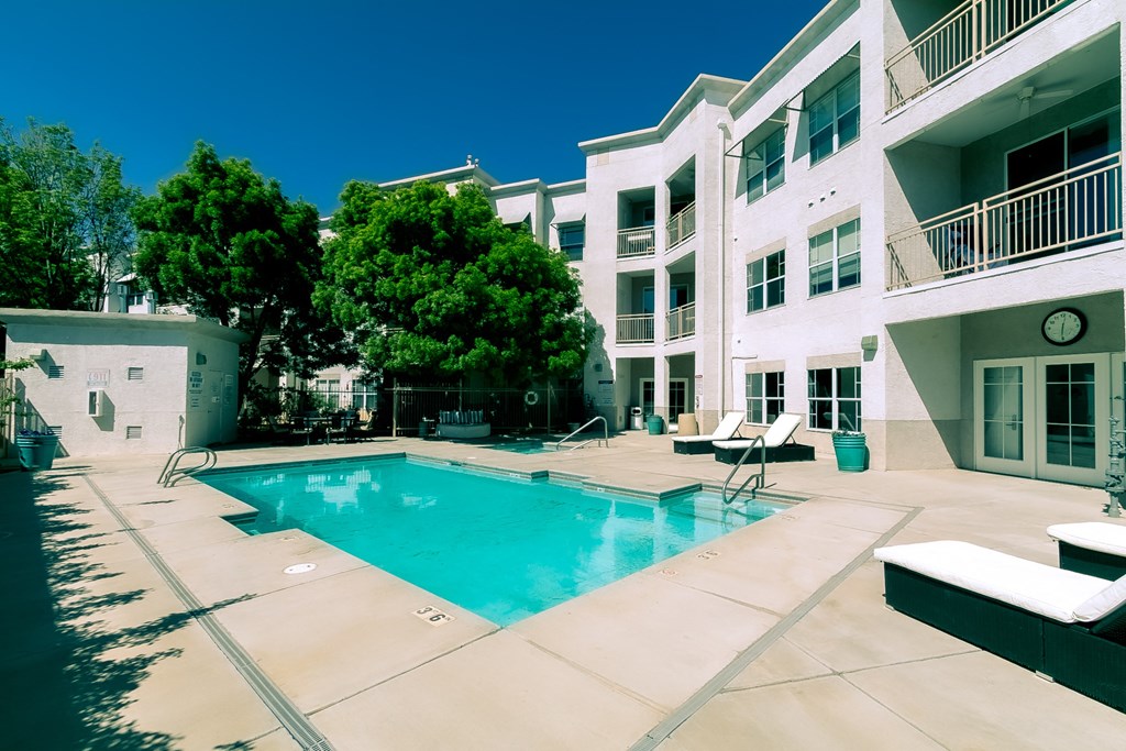a swimming pool with lounge chairs and trees in front of a white building