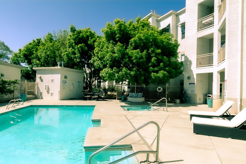 a large swimming pool with a hot tub and lounge chairs next to a building