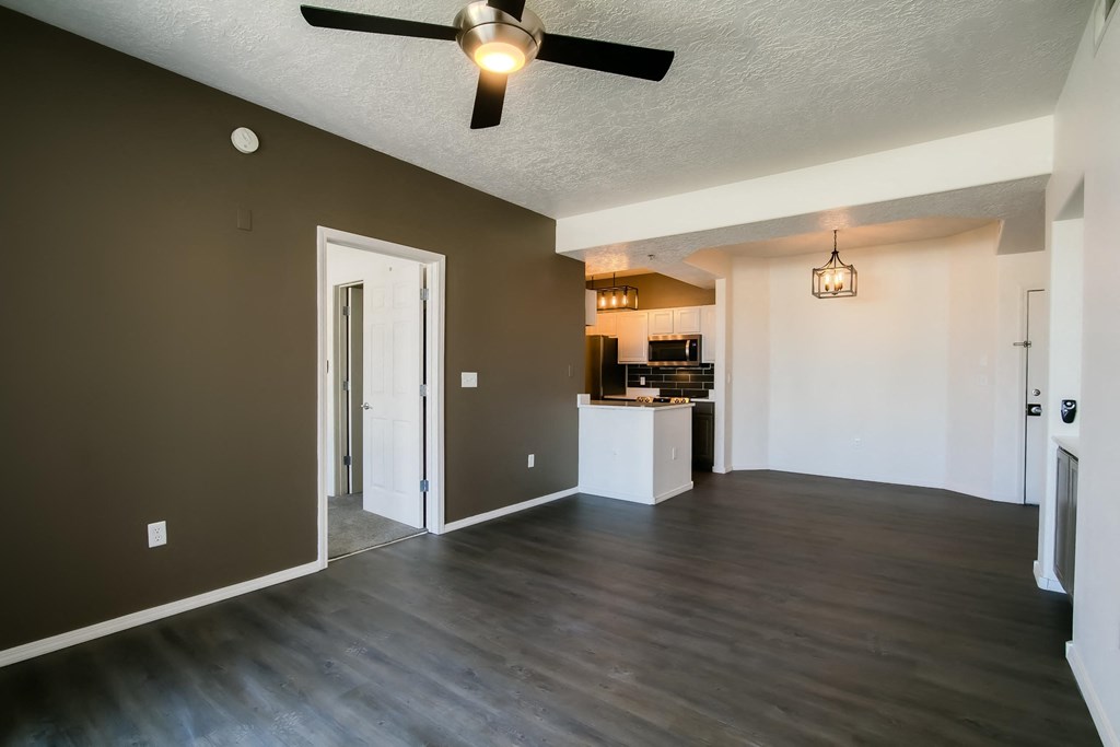 an open living room with a ceiling fan and a kitchen in the background