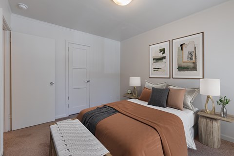 A bedroom with a bed, two lamps, and two framed pictures on the wall at Lake Washington Apartments, 98118