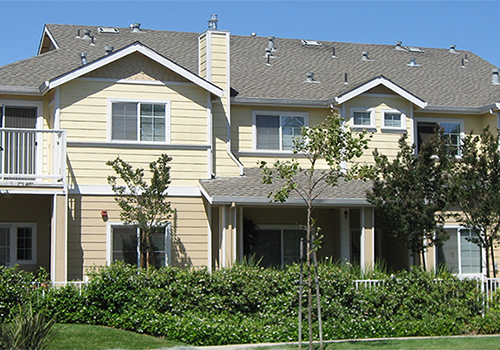 A large, two-story house with a beige exterior and a gray roof.