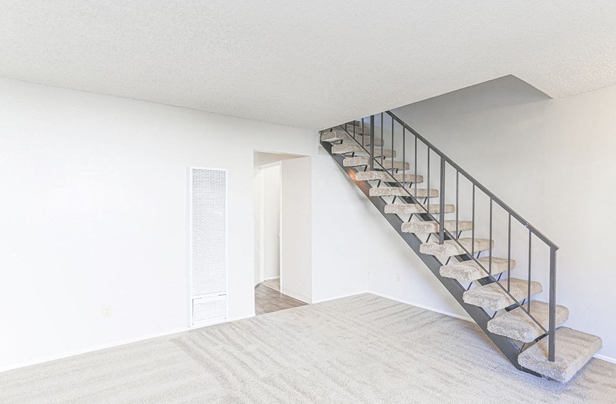 an empty living room with a staircase and a white wall