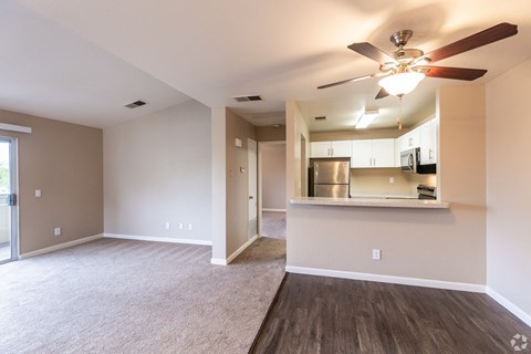 an empty living room with a ceiling fan and a kitchen