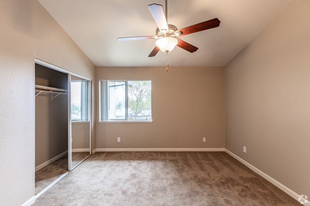 an empty living room with a ceiling fan and a closet