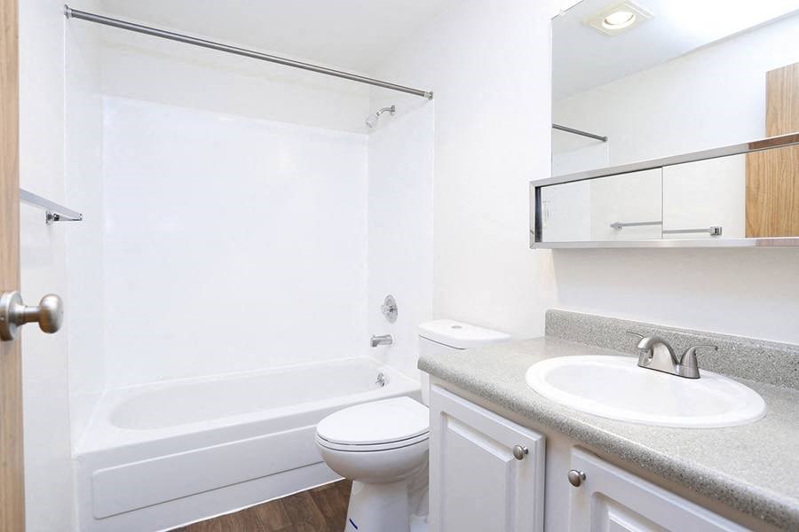 Apartments Des Moines - Marina Club - Bathroom With Granite-Style Countertop, Large Vanity Mirror, White Cabinets, Wood Plank Flooring, and A Shower/Tub Combo