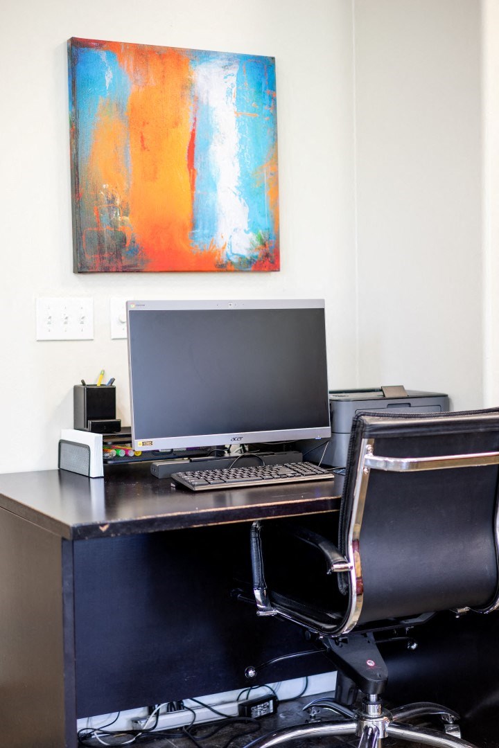 a desk with a computer and a painting on the wall
