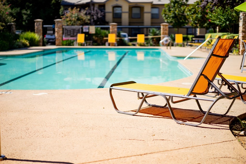 a pair of lounge chairs sit in front of a swimming pool with a building in the background