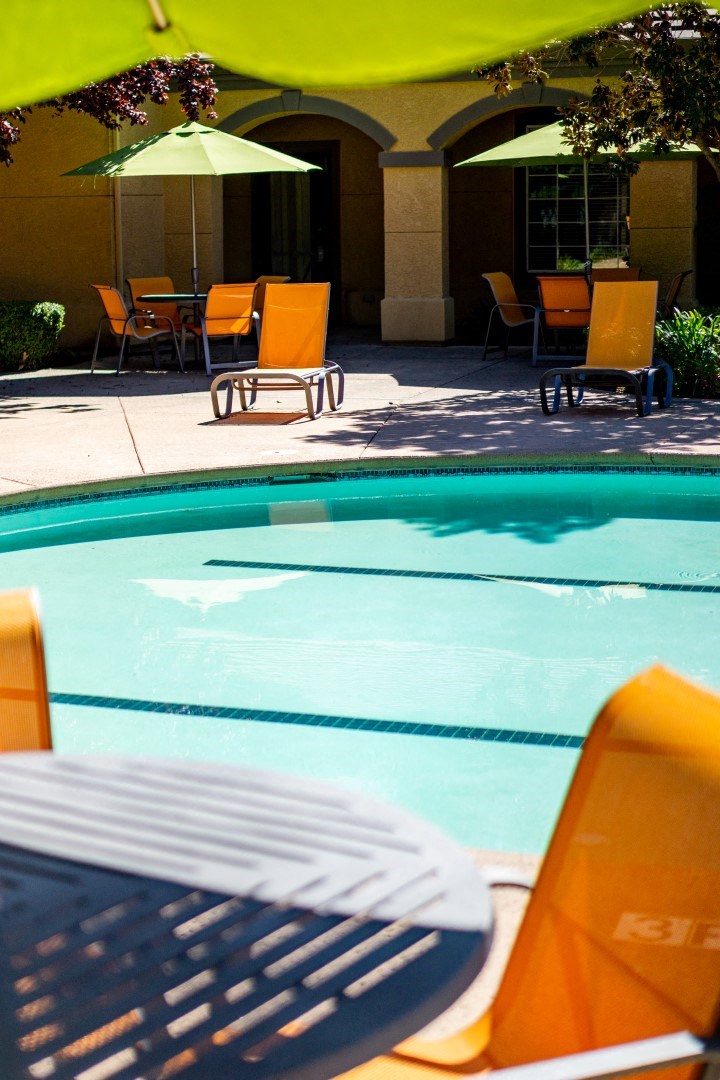 a swimming pool with yellow chairs and umbrellas in the background
