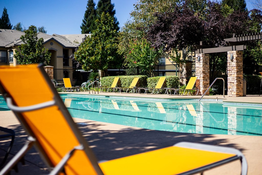a swimming pool with yellow lounge chairs and trees in the background