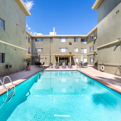 A large swimming pool in the middle of a courtyard surrounded by chairs and buildings.