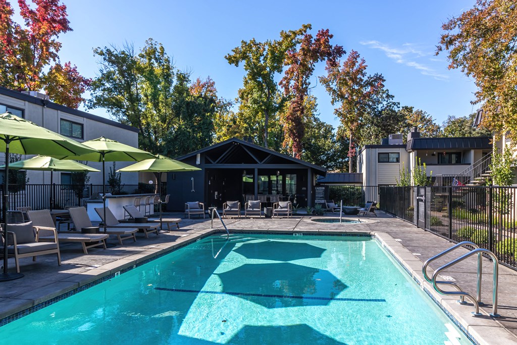 a pool with chairs and umbrellas next to a building and trees