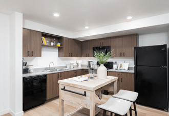 Apartments in Covington for Rent - Station By Vintage - Open Kitchen with Black Appliances, Grey Countertops, Wood-Style Cabinets, and a Free-Standing Island with Two White Barstools