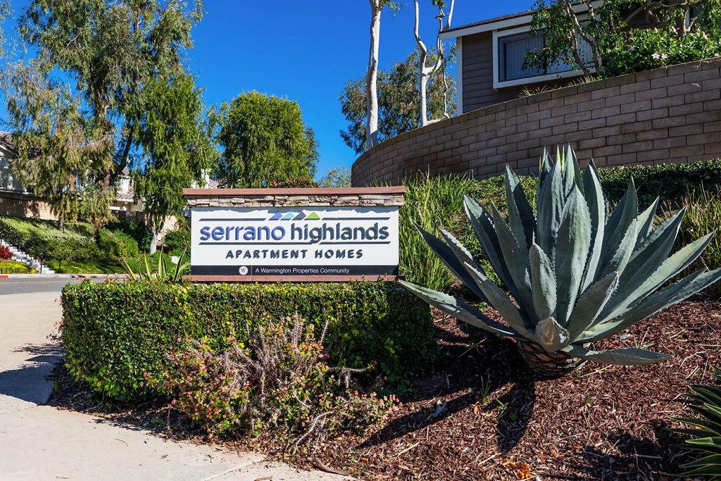 a sign for serrano highlands apartments in front of a plant