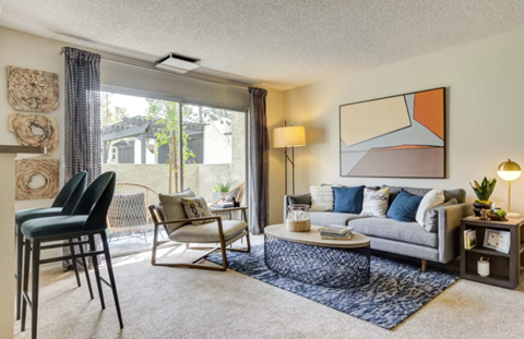 A living room with a grey couch, a chair, a table, and a painting on the wall.
