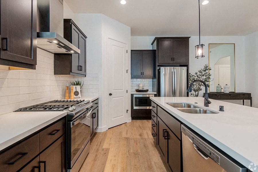 Homes in Oak Park for Rent - Crocker Village - Large Kitchen with Stainless Steel Appliances, Wood-Style Flooring, White Tile Backsplash, Quartz Countertops, Dark Cabinets, and Stylish Decor