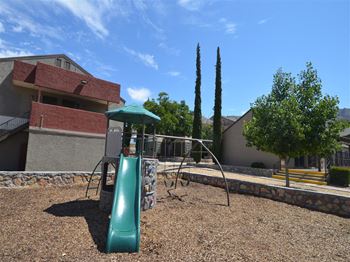 a playground with a slide and swings in front of a building at DESERT PEAKS, EL PASO Texas