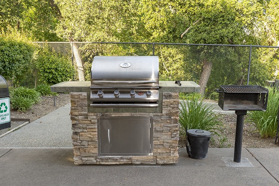 a barbecue grill in a backyard with a trash can