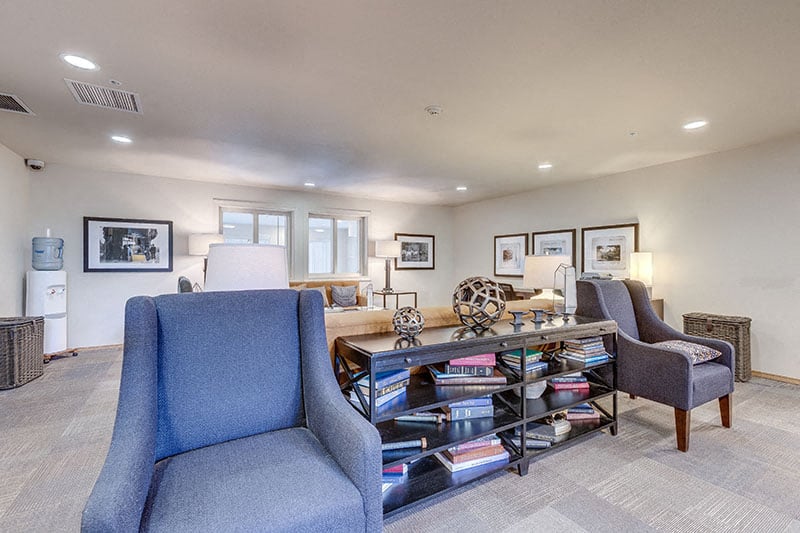 A living room with a grey chair and a bookshelf filled with books.