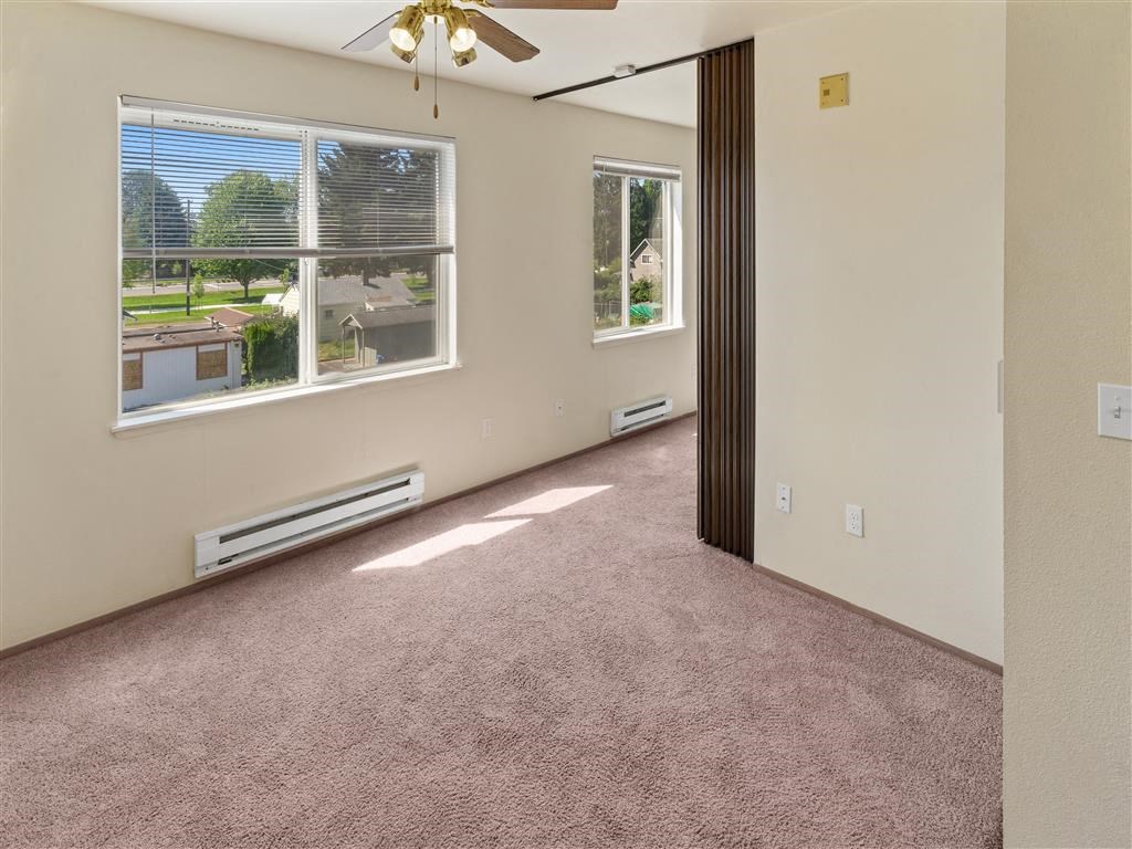an empty room with a ceiling fan and three windows at Webster Court Senior Apartments, Kent, WA
