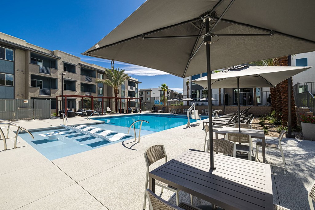 a swimming pool with tables and umbrellas in front of an apartment building at BASE APARTMENT HOMES, LAS VEGAS, Nevada
