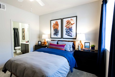 A bedroom with a bed, nightstand, and two framed artworks on the wall.