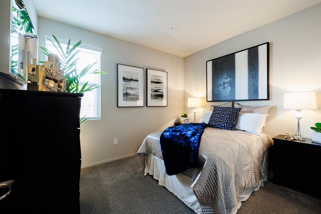 A bedroom with a bed, nightstand, and two framed pictures on the wall.