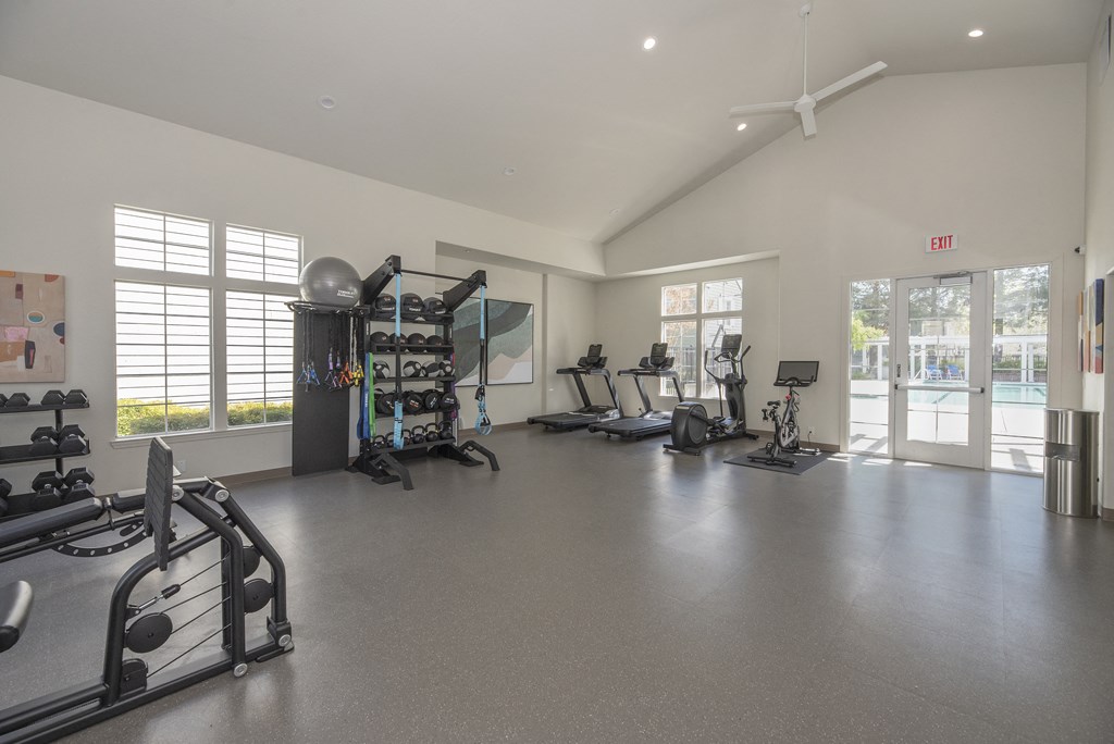a spacious fitness room with exercise machines and windows