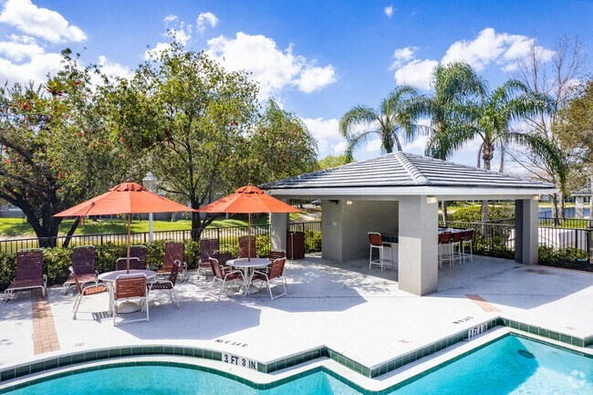 a pool area with umbrellas and chairs and a pool with trees in the background