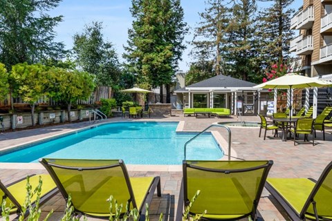 A pool surrounded by green chairs and trees.
