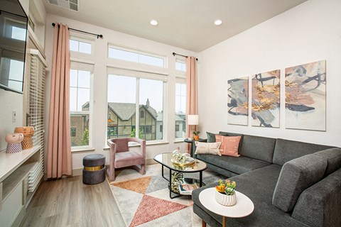 A living room with a grey couch, a pink chair, a small table with a vase of flowers, and a painting on the wall.