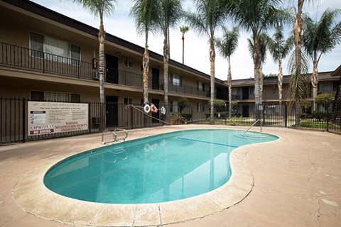 A pool in front of a building surrounded by palm trees.