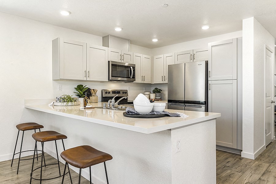 Roseville, CA Rental Homes Near Galleria Mall - Isles - Kitchen with Hardwood-Style Plank Flooring, Stylish Decor, Stainless-Steel Appliances, Quartz Countertops, White Cabinets, and Bar Stools