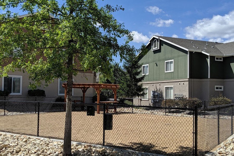 Apartments in Reno for Rent - Sky Vista Commons - Fenced-in Dog Park with Dirt Floor, Gazebo, and Table, Surrounded by Green Trees and Apartment Building
