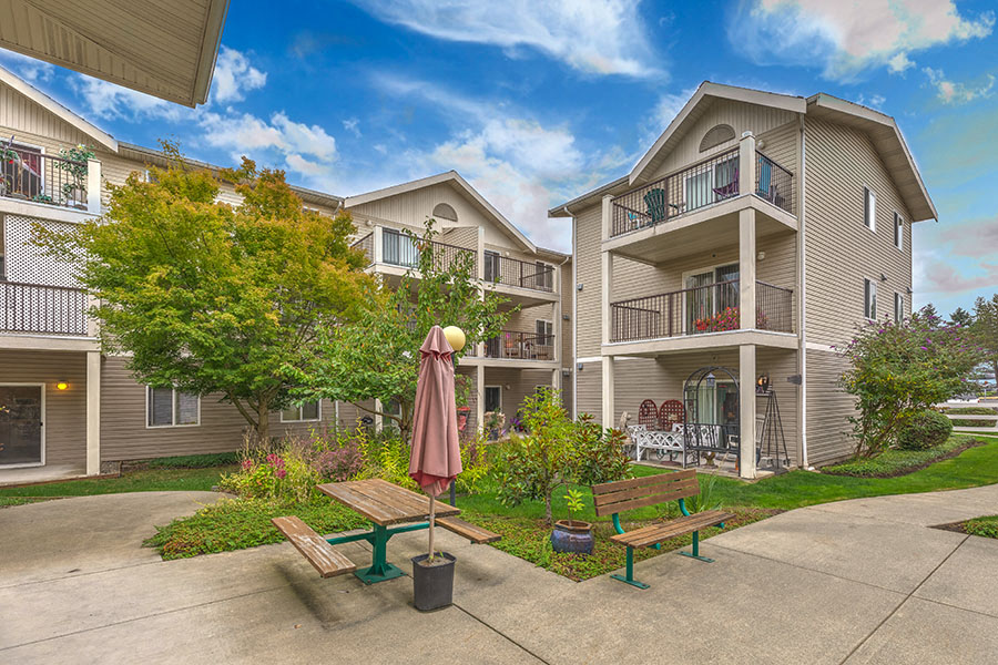 A sunny day at a residential complex with a bench and table in the foreground.