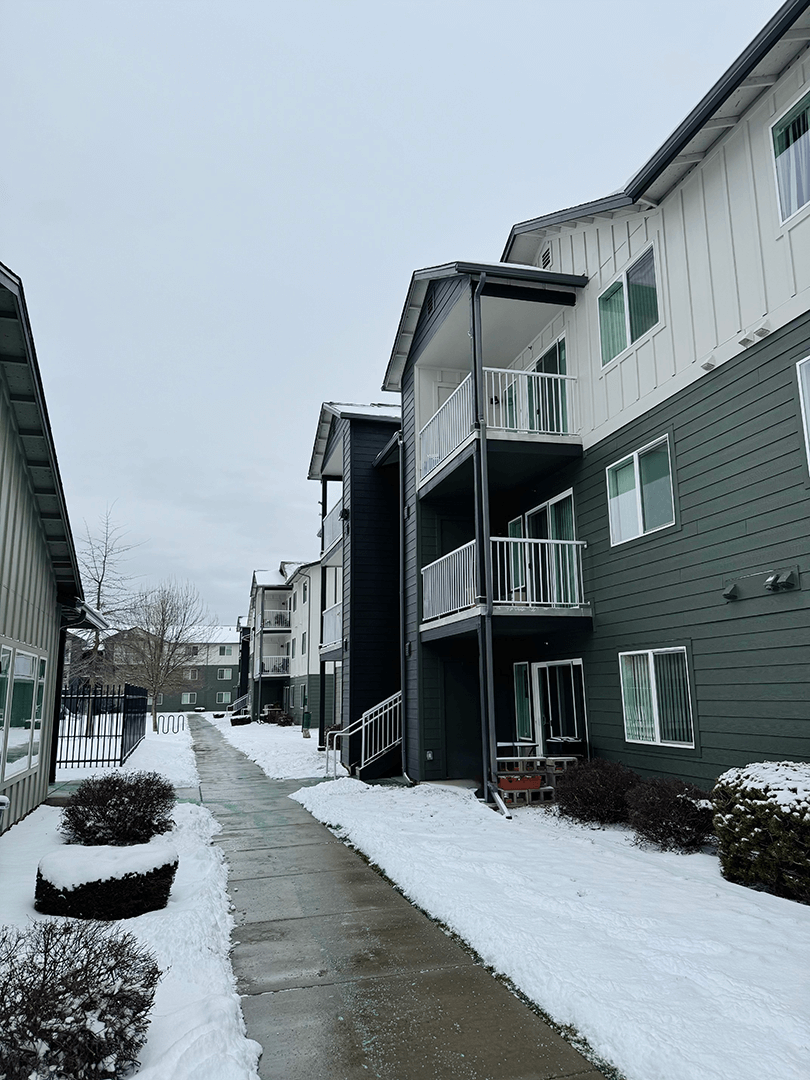 A snow-covered walkway leads to a building with a balcony A snow-covered walkway leads to a building with a balcony at Falls Creek Apartments in 83815