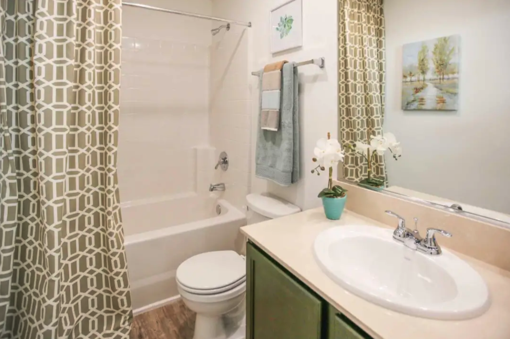 Apartments Sparks, NV - Fountainhouse at Victorian Square - Bathroom With Wood Style Flooring, Granite Slab Countertop With Stainless Steel Sink, Large Vanity Mirror, Toilet, And A Shower With Bathtub