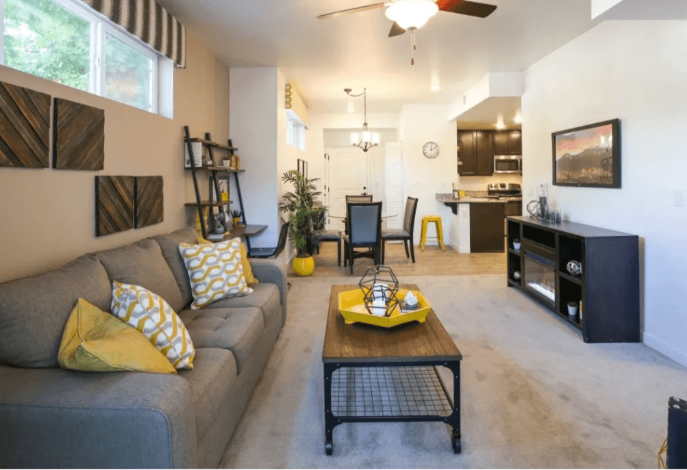 Sparks, NV Apartments - Fountainhouse at Victorian Square - Living Room With High Ceiling, Dual Pane Vinyl Windows With Blinds, Carpet Flooring, Ceiling Fan, And Access To Dining And Kitchen Area
