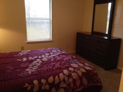 A bed with a purple comforter sits in a bedroom with a large mirror.