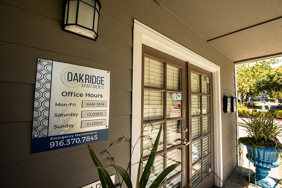 the front door of oak ridge apartments with a sign for the office hours