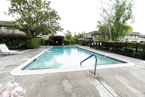a swimming pool with a fence and trees in the background at OTAVON APARTMENTS, Novato, CA 94947