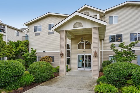 A beige building with a front entrance and bushes.