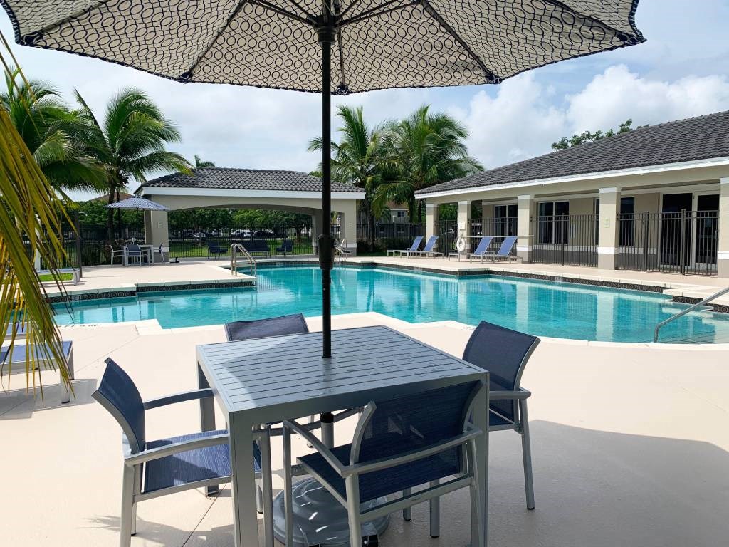 Resort style pool and umbrella with chairs at Tuscany Place Apartments, Homestead 